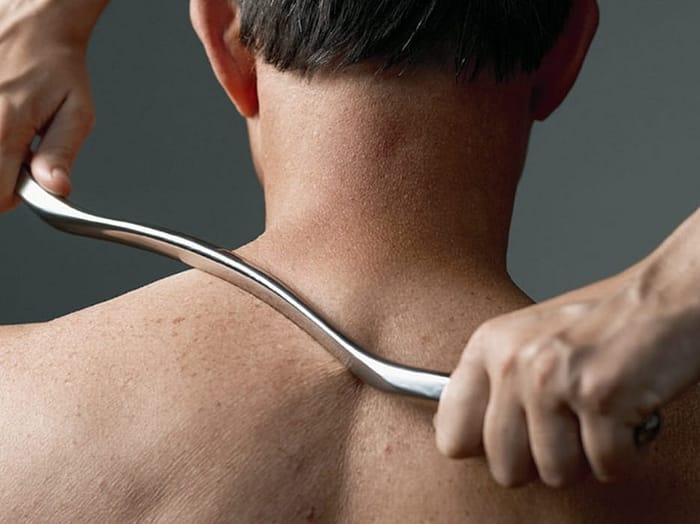 Person receiving IASTM therapy with a specialized instrument gliding over the neck area, demonstrating soft tissue mobilization technique for pain relief and improved mobility.