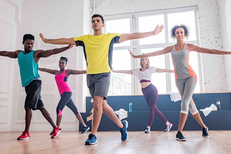 Group of diverse individuals participating in a Zumba fitness class, showcasing movement and energy in a bright, spacious studio, emphasizing wellness and rehabilitation through exercise.