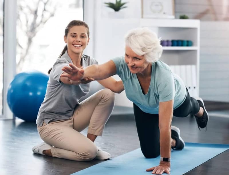 Senior woman engaging in rehabilitation exercises with a therapist, focusing on strength and balance improvement in a wellness center.