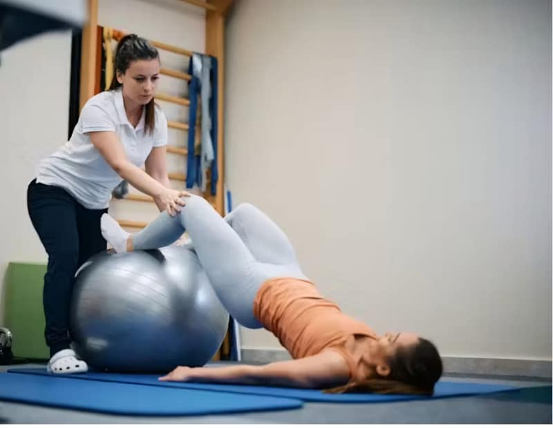 Physical therapist assisting a patient in therapeutic exercises on a stability ball, enhancing mobility and strength in a rehabilitation setting.